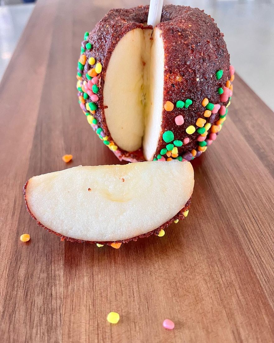 A candy-coated apple covered in coloured sprinkles, sliced open on a wooden board.