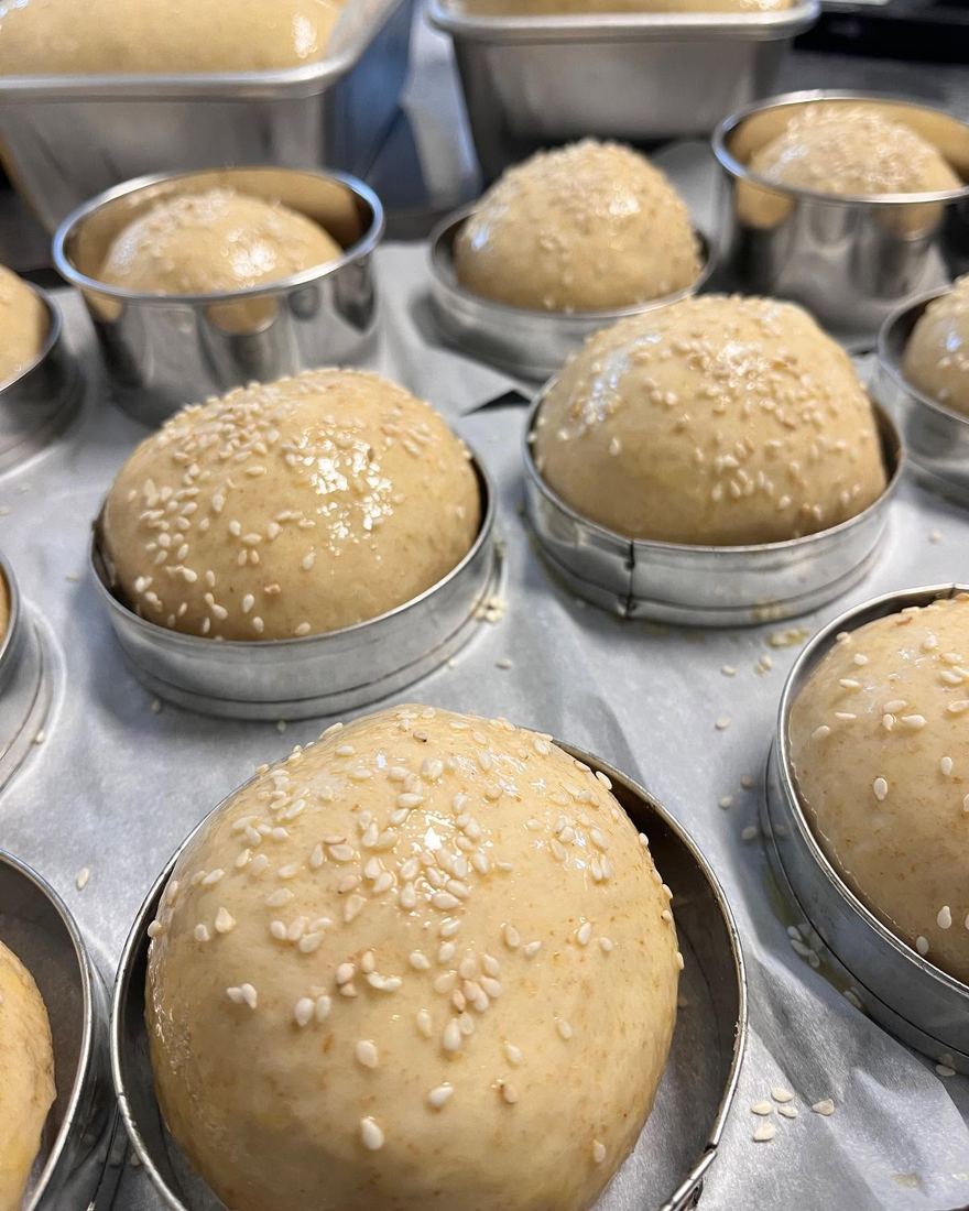 Rounds of seeded dough resting in metal tins, ready for the oven.