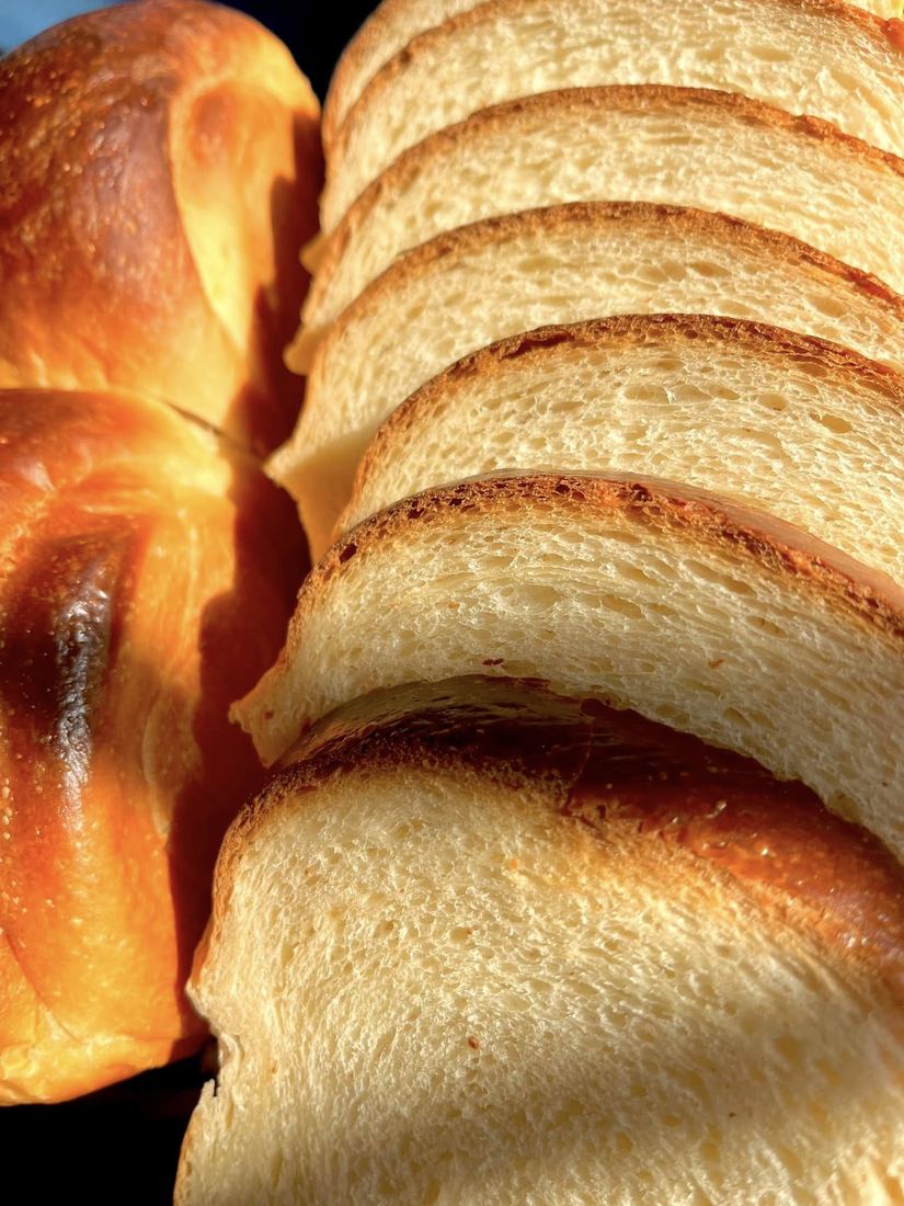 A golden, braided loaf beside thick slices of soft white bread, lit by warm afternoon light.