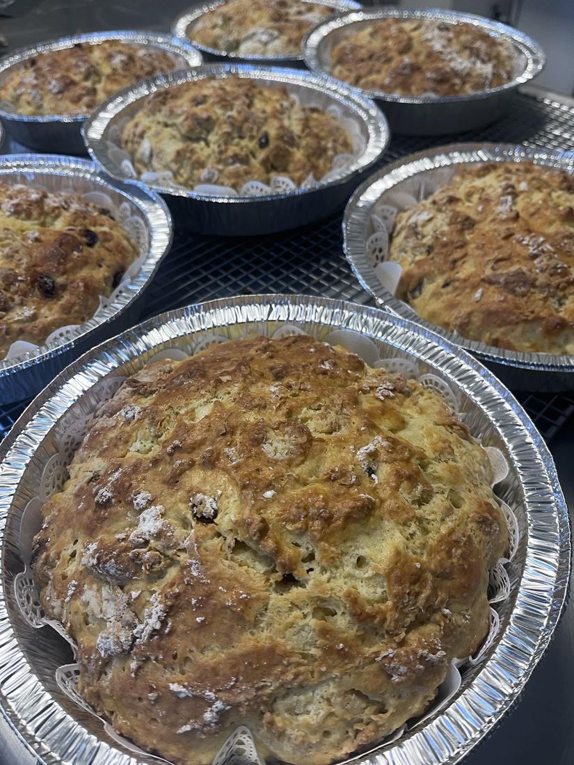 Round loaves studded with fruit, baked in foil pans and cooling on a rack.