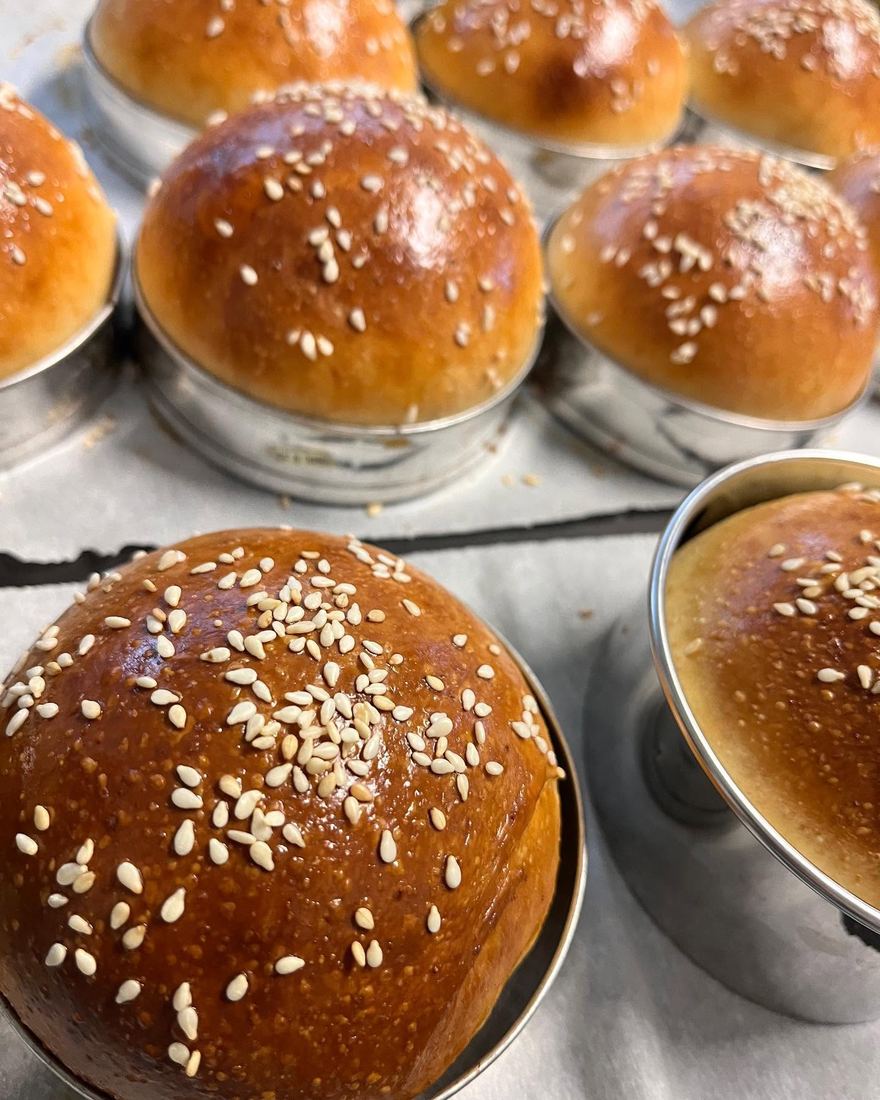 Close view of golden sesame-seeded rolls resting in round metal tins.