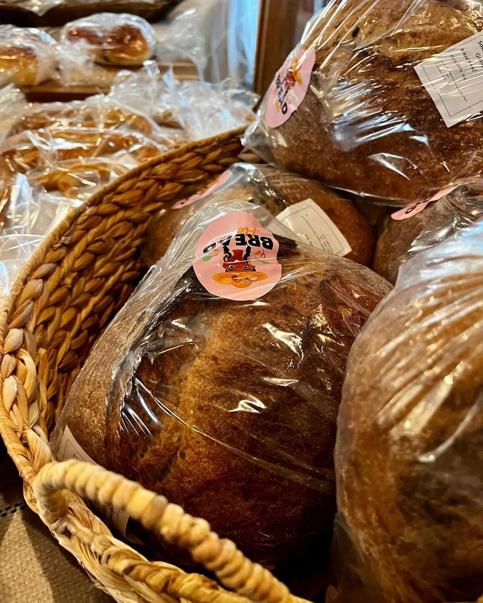 Wrapped loaves and pastries arranged in a woven basket on the bakery shelf.
